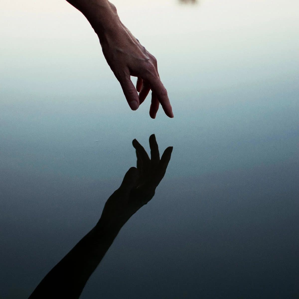 A hand meeting its reflection on the water